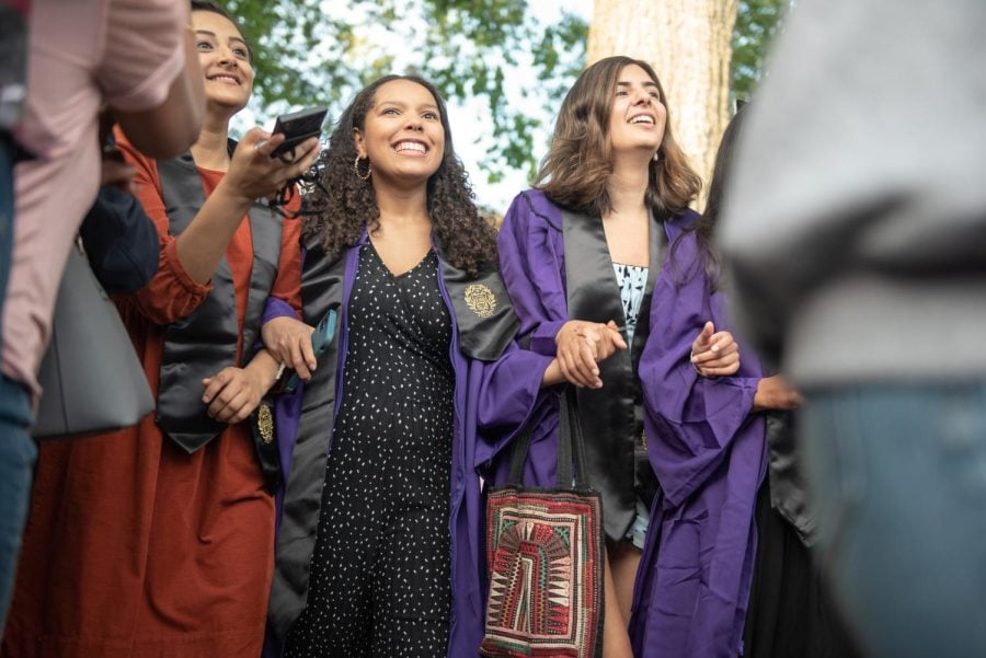 Two people in purple graduation gowns and black stoles walk together, holding each other’s hands and smiling.