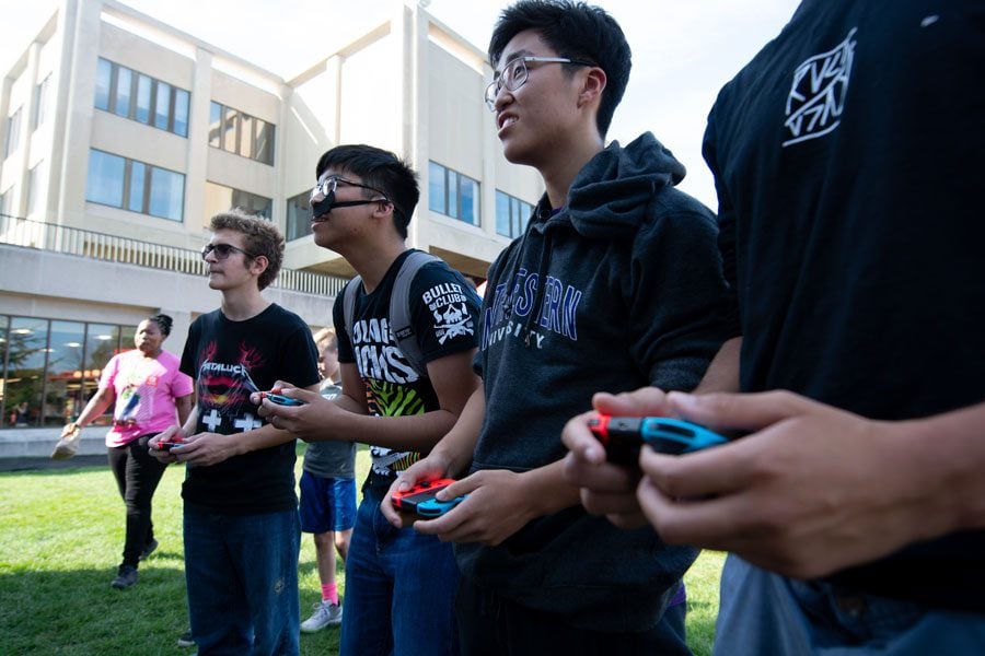 Four Northwestern students in black hoodies play their red-and-blue Nintendo Switch consoles outside on the Norris University Center East Lawn.