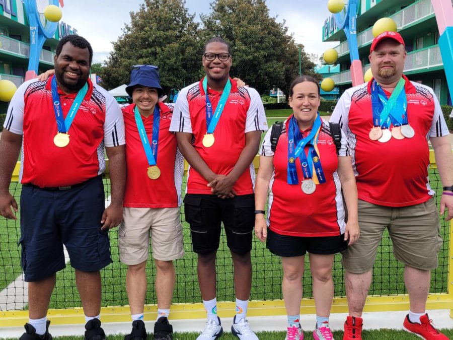 Athletes stand side by side, wearing matching red polos with medals around their necks.