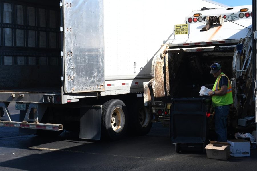 A worker in a neon vest examines a plastic bag in front of a recycling truck.