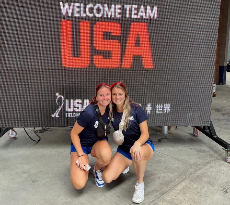Two women with red bandanas in their hair and matching navy “Team USA” T-shirts stand by a “Team USA” sign.