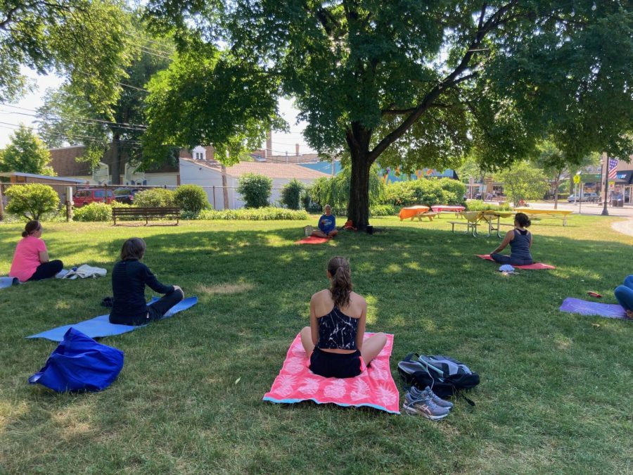 Participants sit on yoga mats in the grass facing an instructor.
