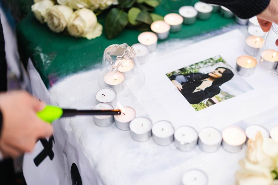 A photo of an Iranian woman surrounded by small candles arranged in a heart shape on top of a green-and-white embankment.