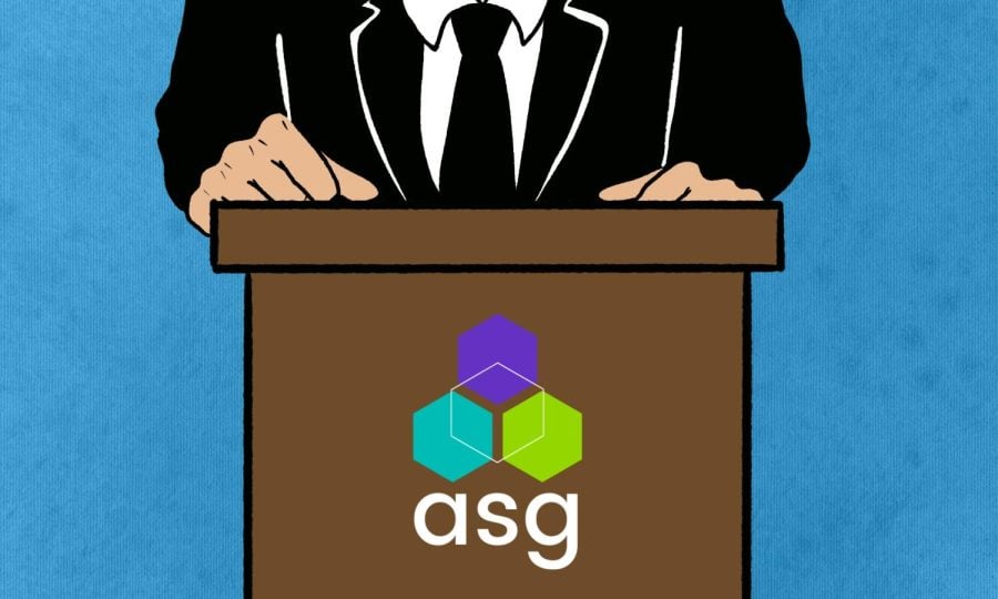 An individual in a suit and tie behind an brown podium featuring the ASG logo.