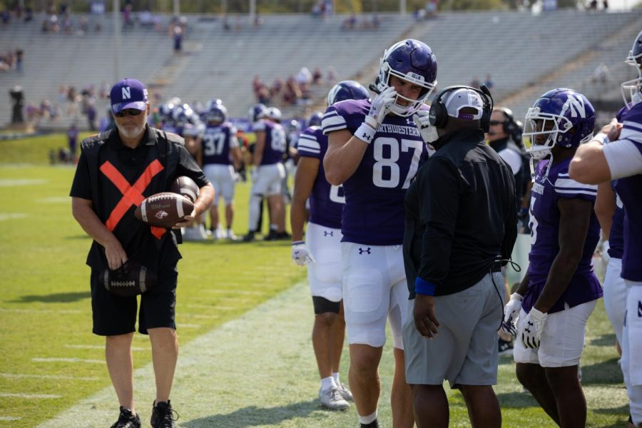 Player in purple uniform adjusts helmet on sideline.
