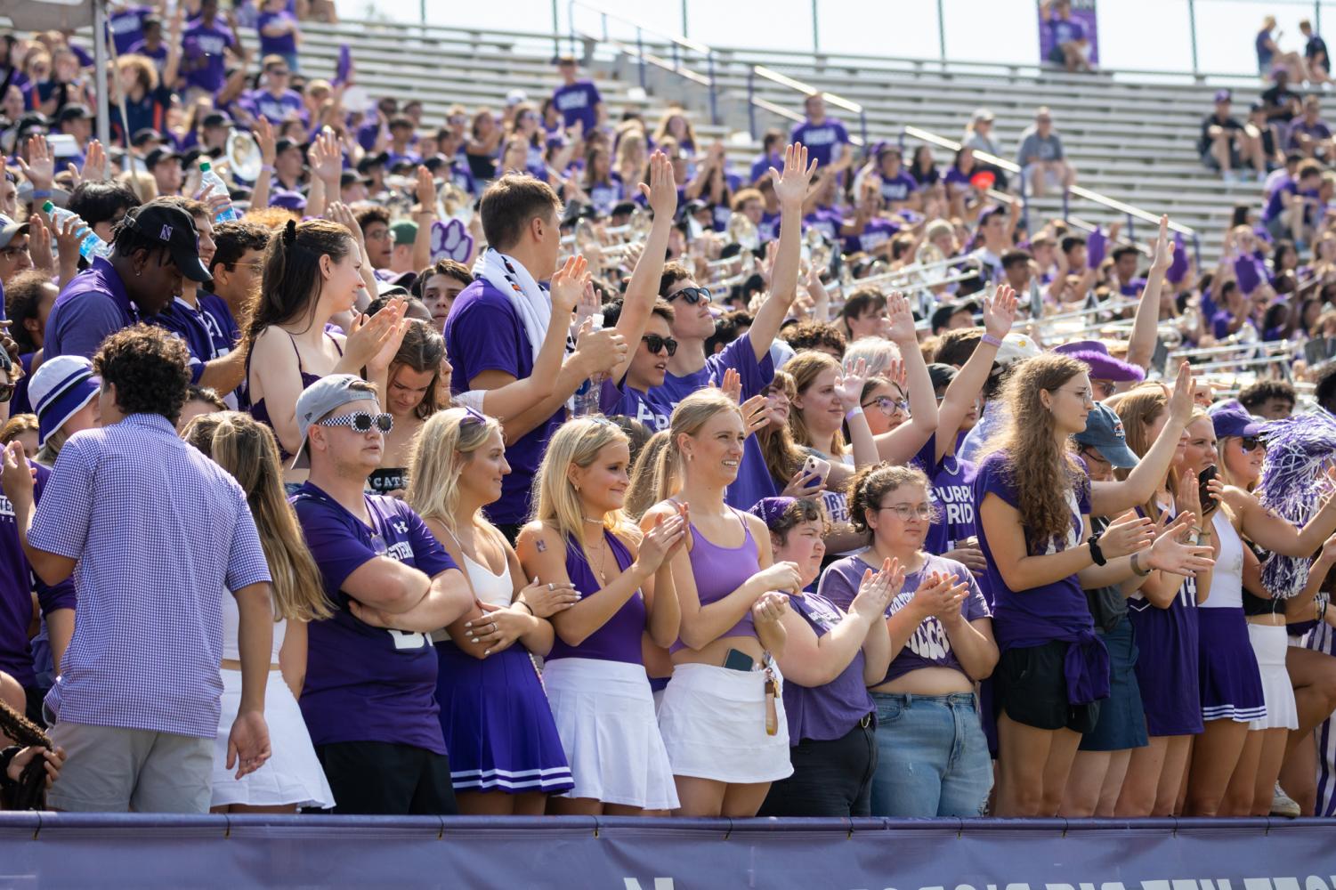 People dressed in purple cheer in the stands of a football stadium.
