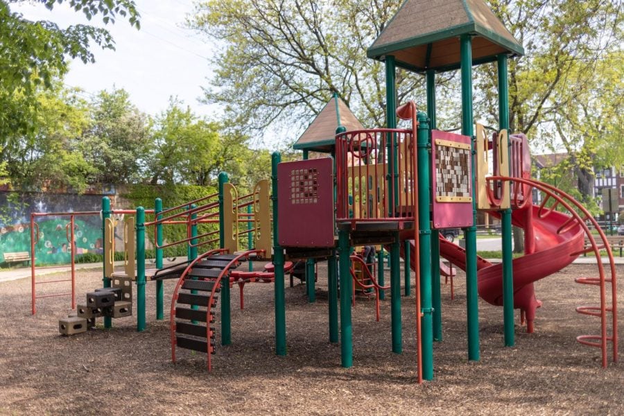 A red playground structure in the foreground against a brown background and trees.