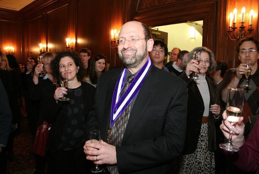 Man with medal around his neck surrounded by crowd toasting their glasses to him.