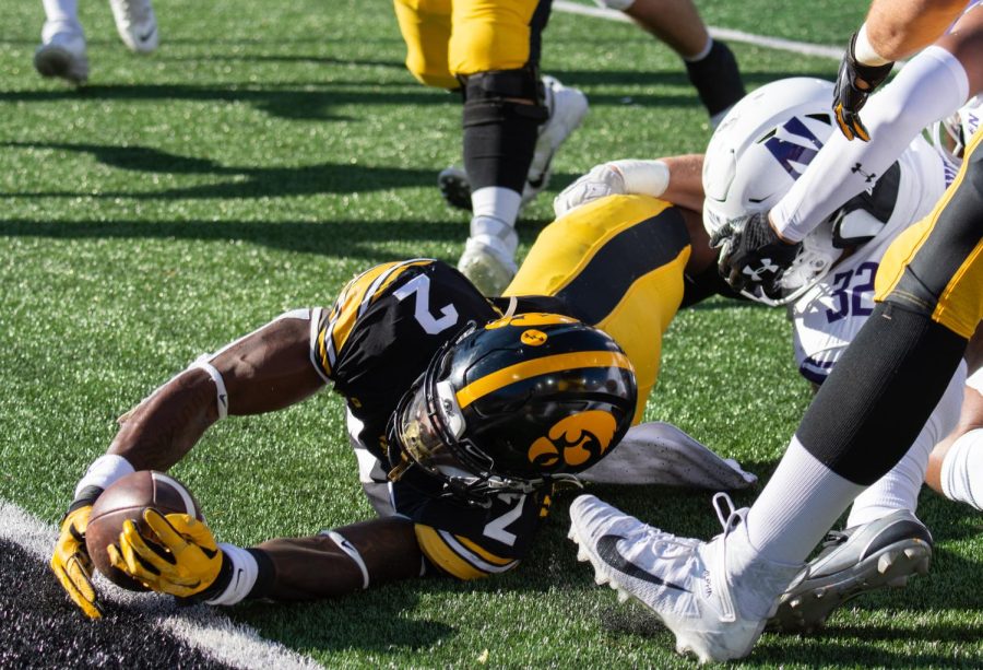 A football player wearing black and yellow dives over the line to score a touchdown.