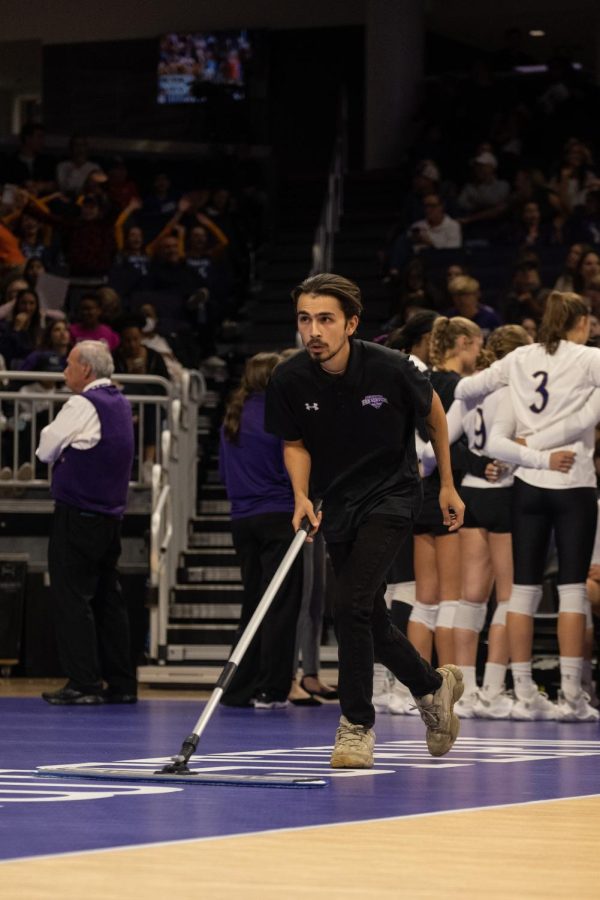 A person in a black uniform pushes a broom across a volleyball court.