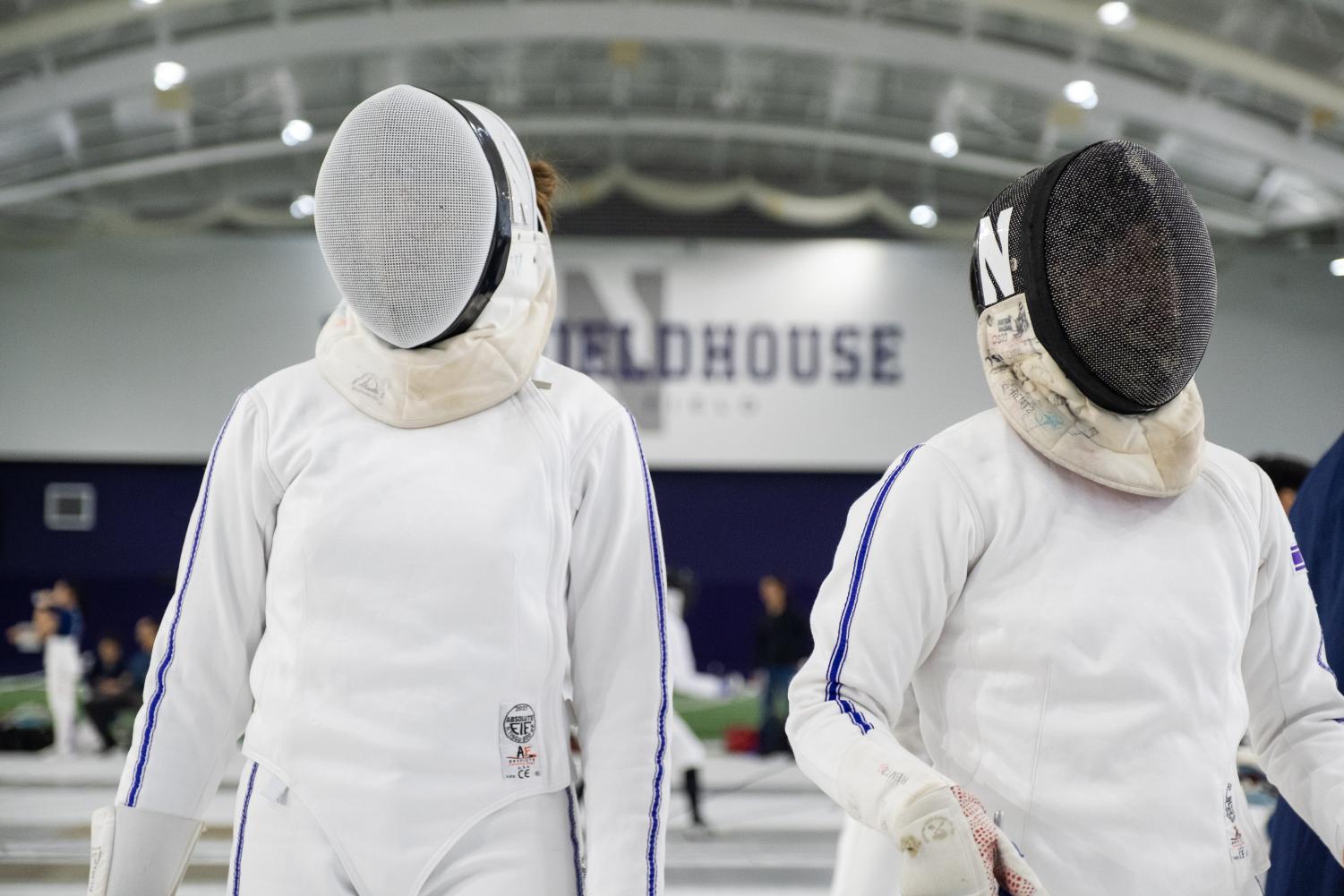 Two fencers wearing masks stand side by side.