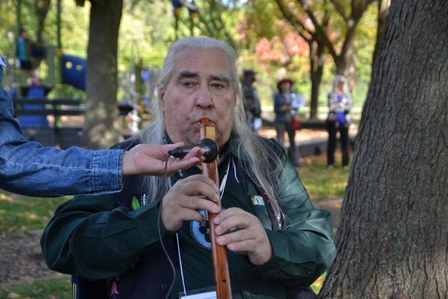 Man with long hair holds a wooden flute in a park.