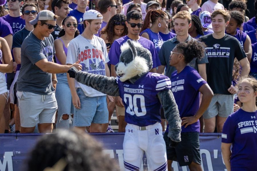 A mascot fist-pumps a fan in the stands at a football game.