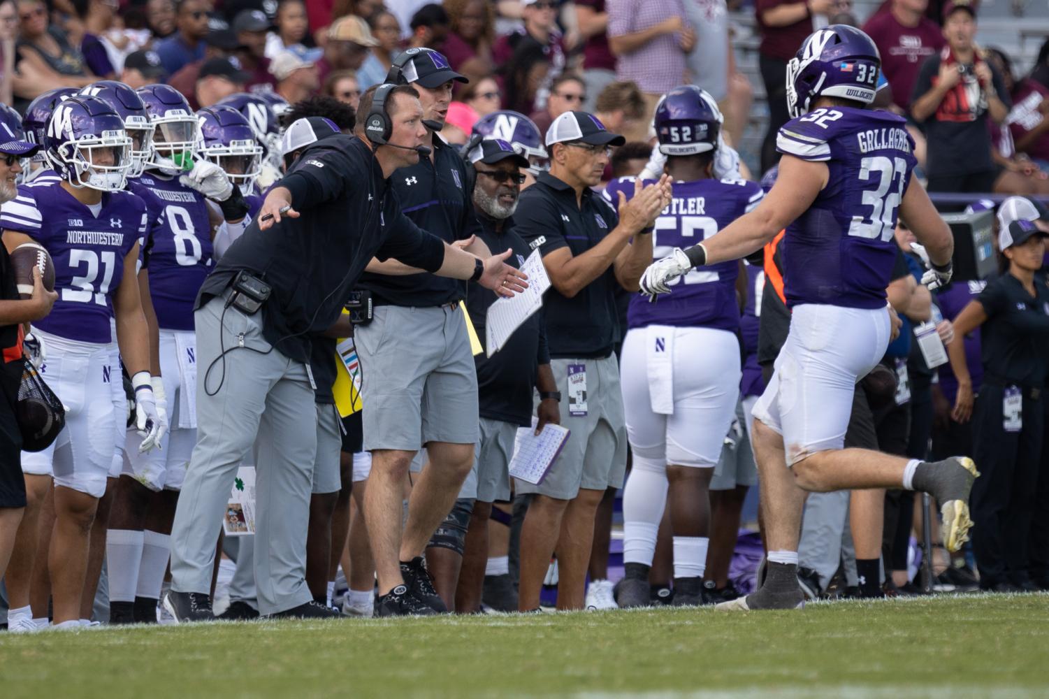 Coaches+in+black+shirts+talk+to+football+players+in+purple+jerseys+on+the+sideline.