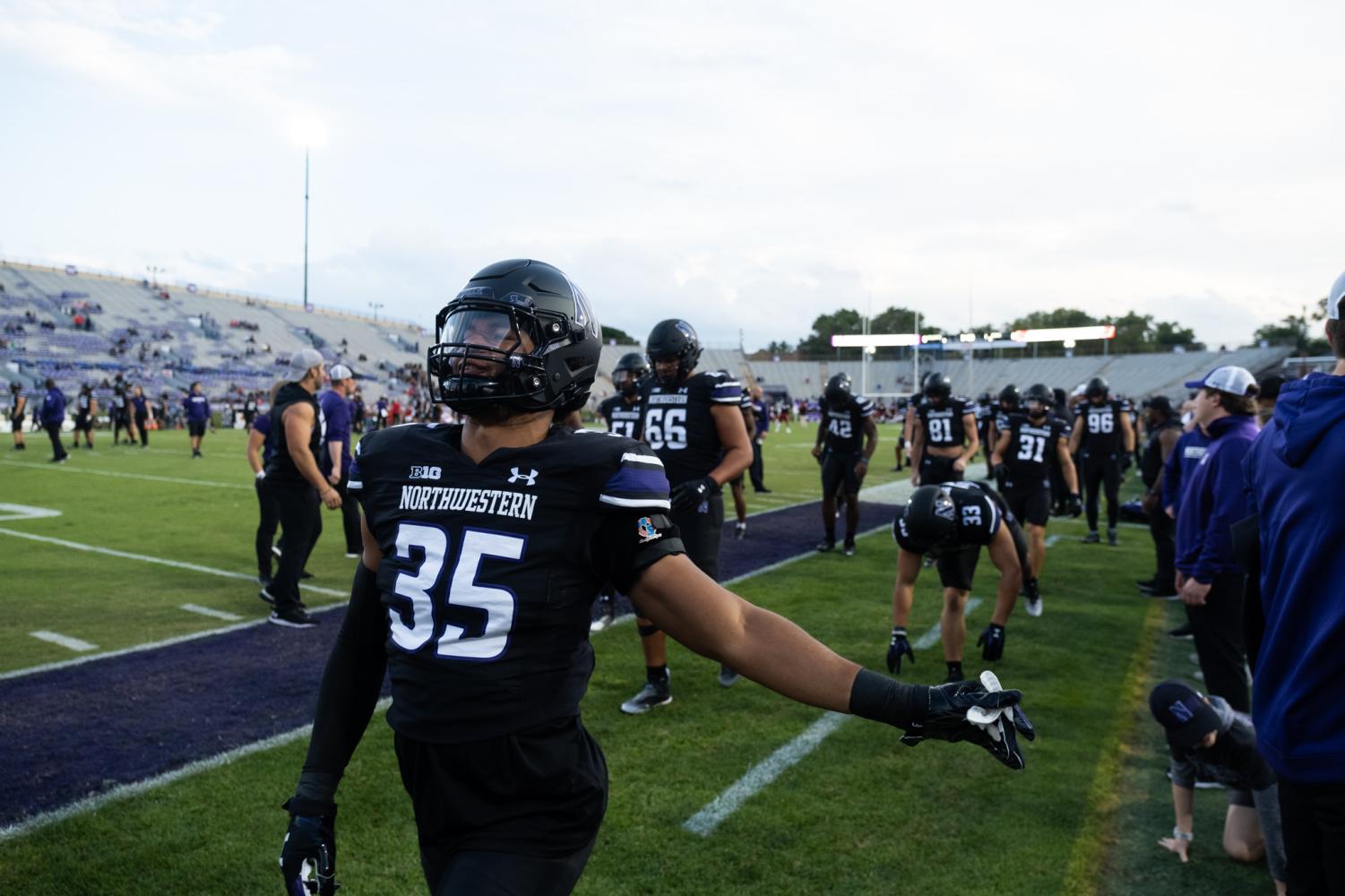 Players+in+black+uniforms+and+black+helmets+stretch+on+a+football+field+sideline.