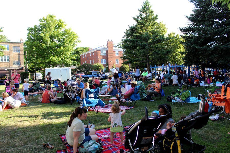 Over 30 adults and children sitting on blankets and lawn chairs at an open grassy area in a park.