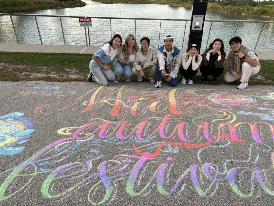 Students+crouch+in+front+of+a+lake+with+%E2%80%9CMid-Autumn+Festival%E2%80%9D+written+in+rainbow-colored+chalk+in+front+of+them.