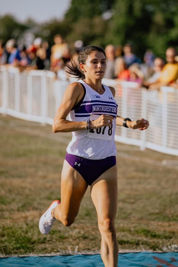 A girl with brown hair in a white jersey runs across a finish line