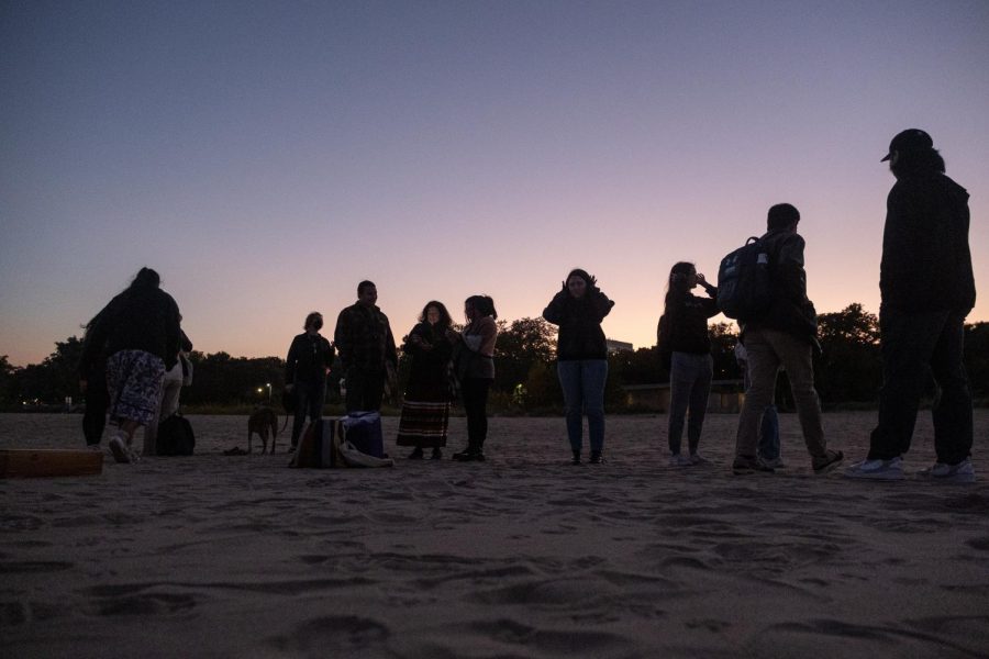 Northwestern students, professors and community members stand on a beach silhouetted against the sunset.