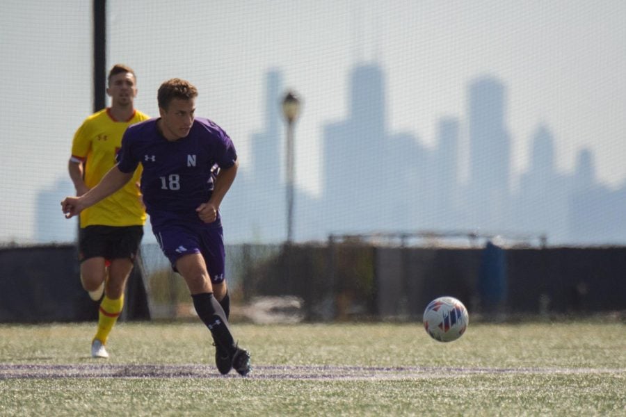 An athlete in a purple jersey kicks a ball with a city skyline in the background.