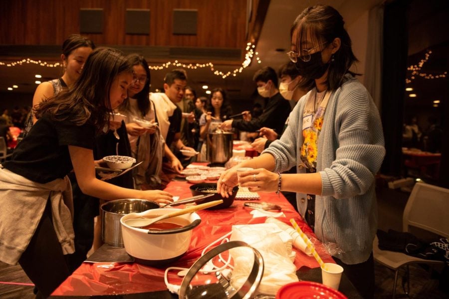 A student gets food in a lit-up room, decorated with red tablecloths and lanterns.