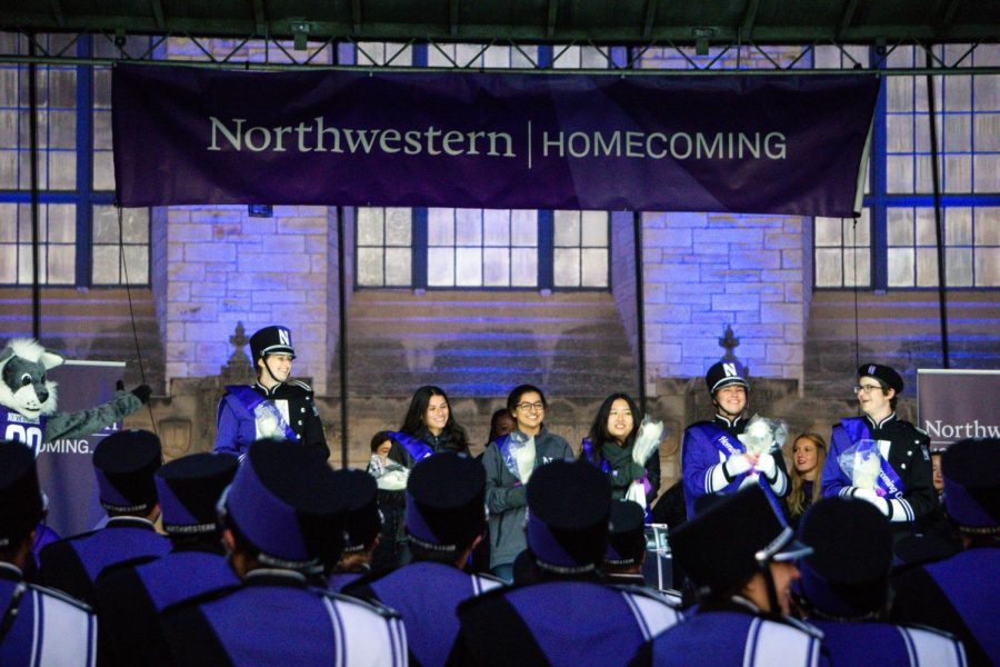 Three people in band uniforms, five other people and a person in a wildcat costume stand on stage. Two people are holding flowers.