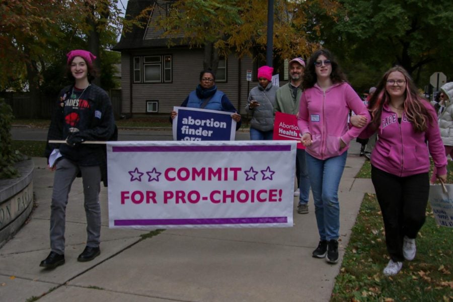 Three people hold a sign with the words “Commit for Pro-Choice!”