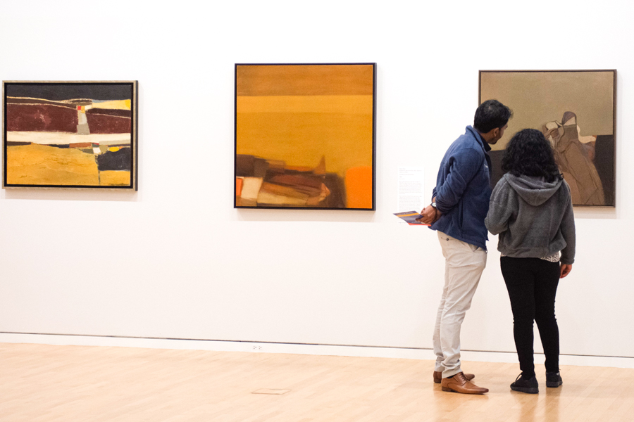 Two people examine one of three paintings on the wall of the Block Museum of Art.