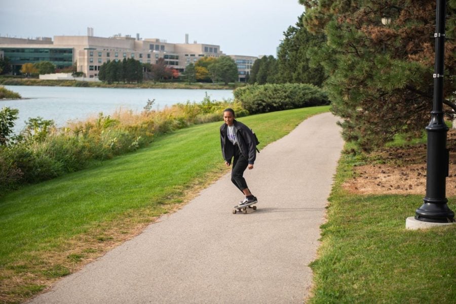 A person is photographed riding their skateboard on a pathway next to the Lakefill.
