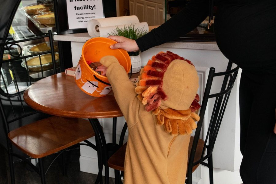 A person tilts down an orange bucket filled with candy for a child wearing a lion costume to reach.