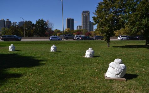 White sculptures on a green field in front of several buildings.