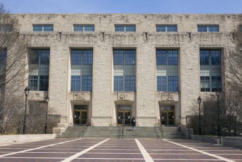 A building with three sets of doors with windows above them and stairs in front of them, including a person walking up the stairs.