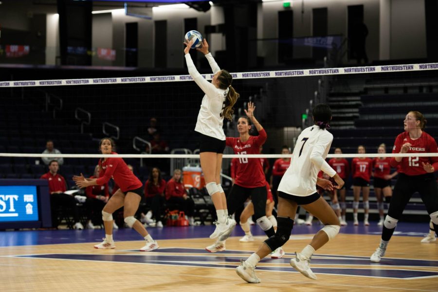 A player wearing a white jersey with the number ‘5’ on it sets a volleyball.