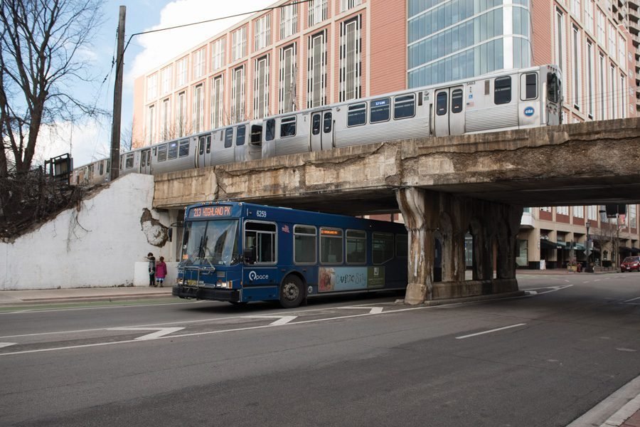 A Pace bus passes under a bridge while a CTA “L” train crosses above.