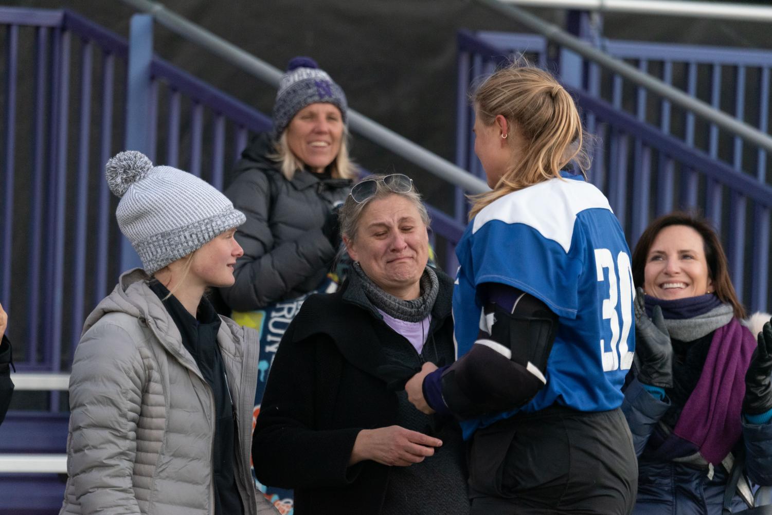 A person standing next to a field hockey player smiles while crying.
