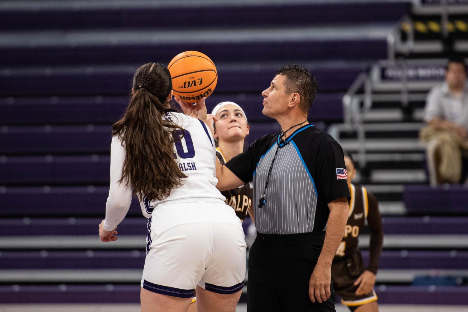 A referee holds a basketball between two athletes.