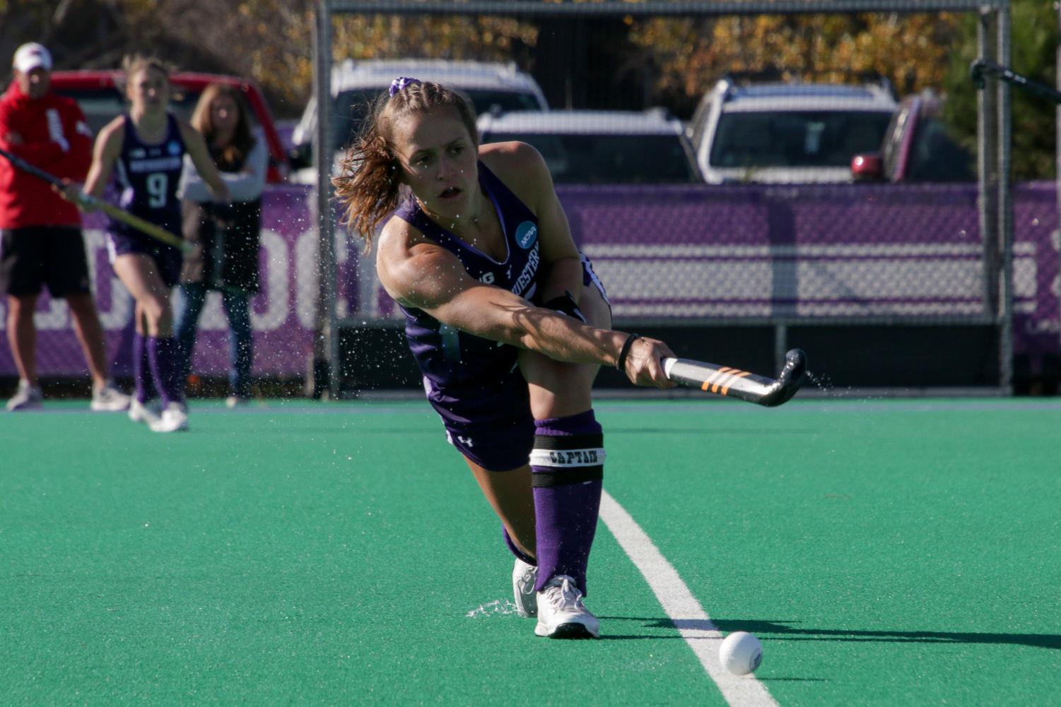A field hockey player swings their stick to hit the ball.