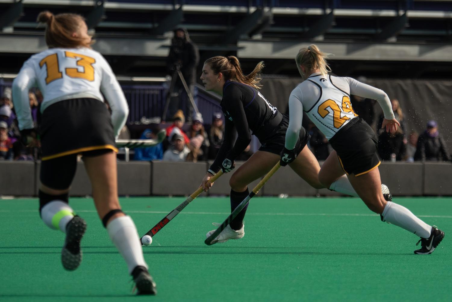 A field hockey player in a black jersey runs and keeps the ball away from players in white jerseys.