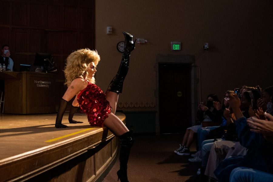 Alyssa Edwards leans on a stage in front of an audience with a leg lifted in the air.