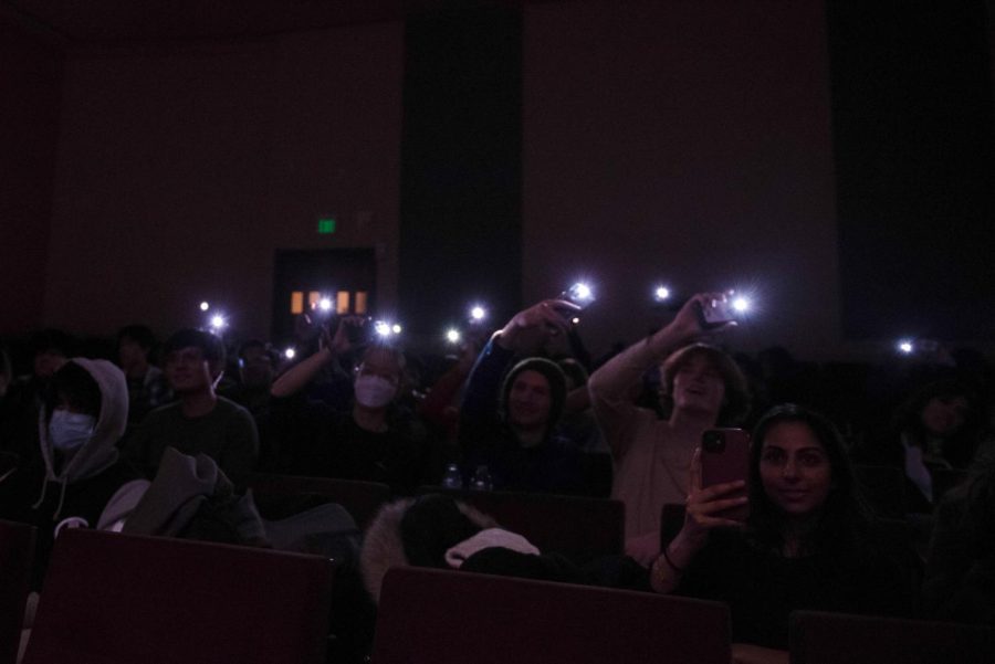 In a darkened room, audience members wave their phone flashlights.
