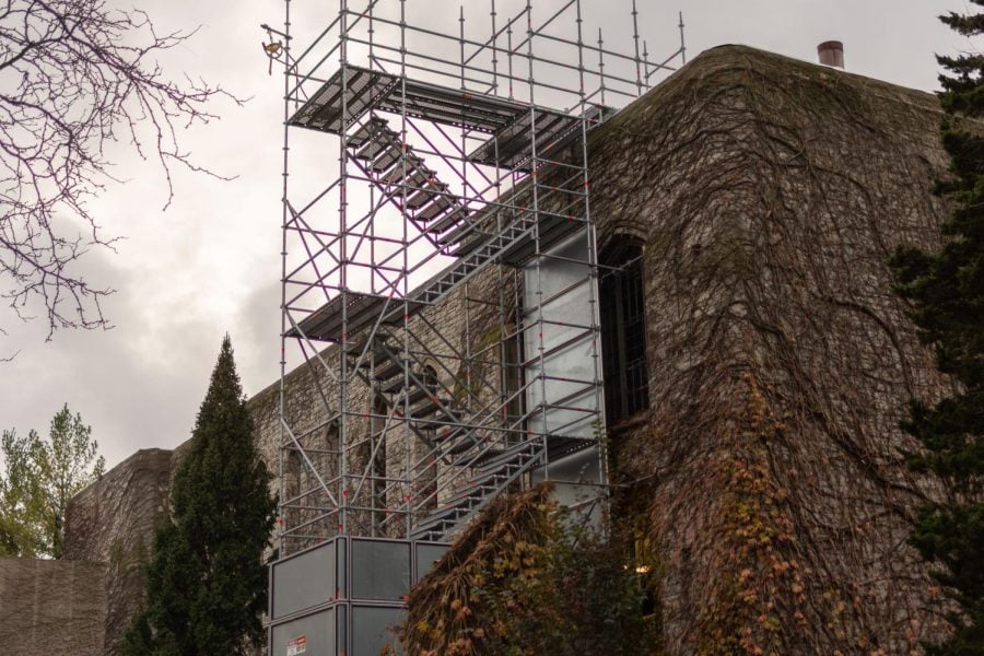 A picture of metal scaffolding scaling a brick building with vines and leaves growing on the side.