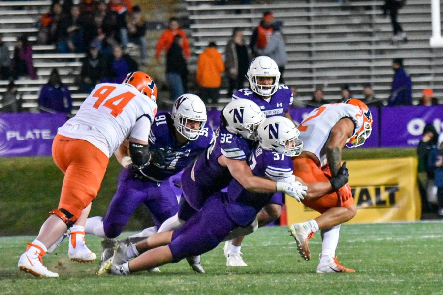 Players in purple jerseys tackle player in white jersey on a field.