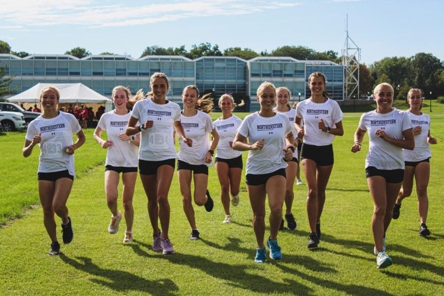 Athletes in white shirts run on a cross country course.