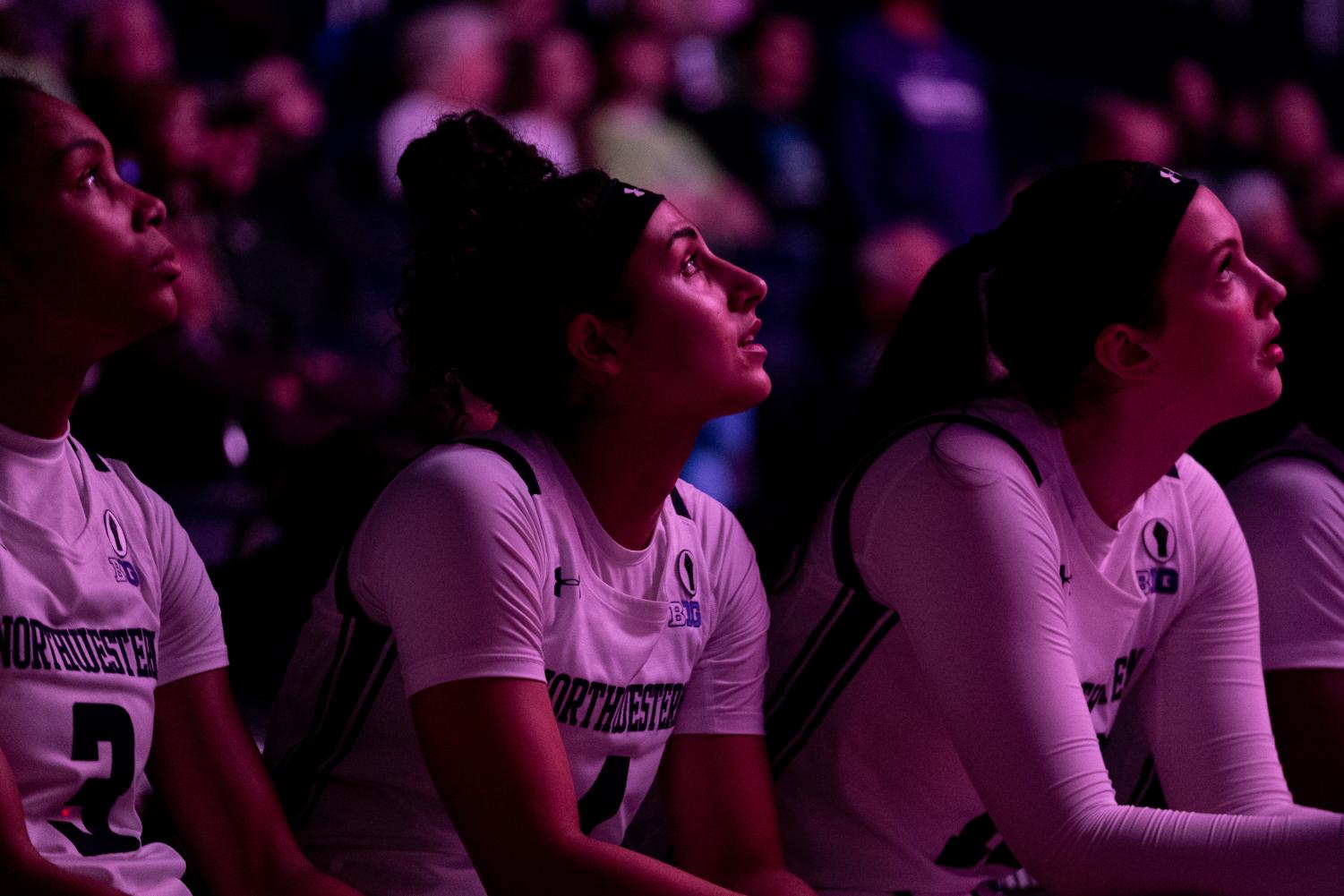 Three athletes sit and look up in dim purple lighting.