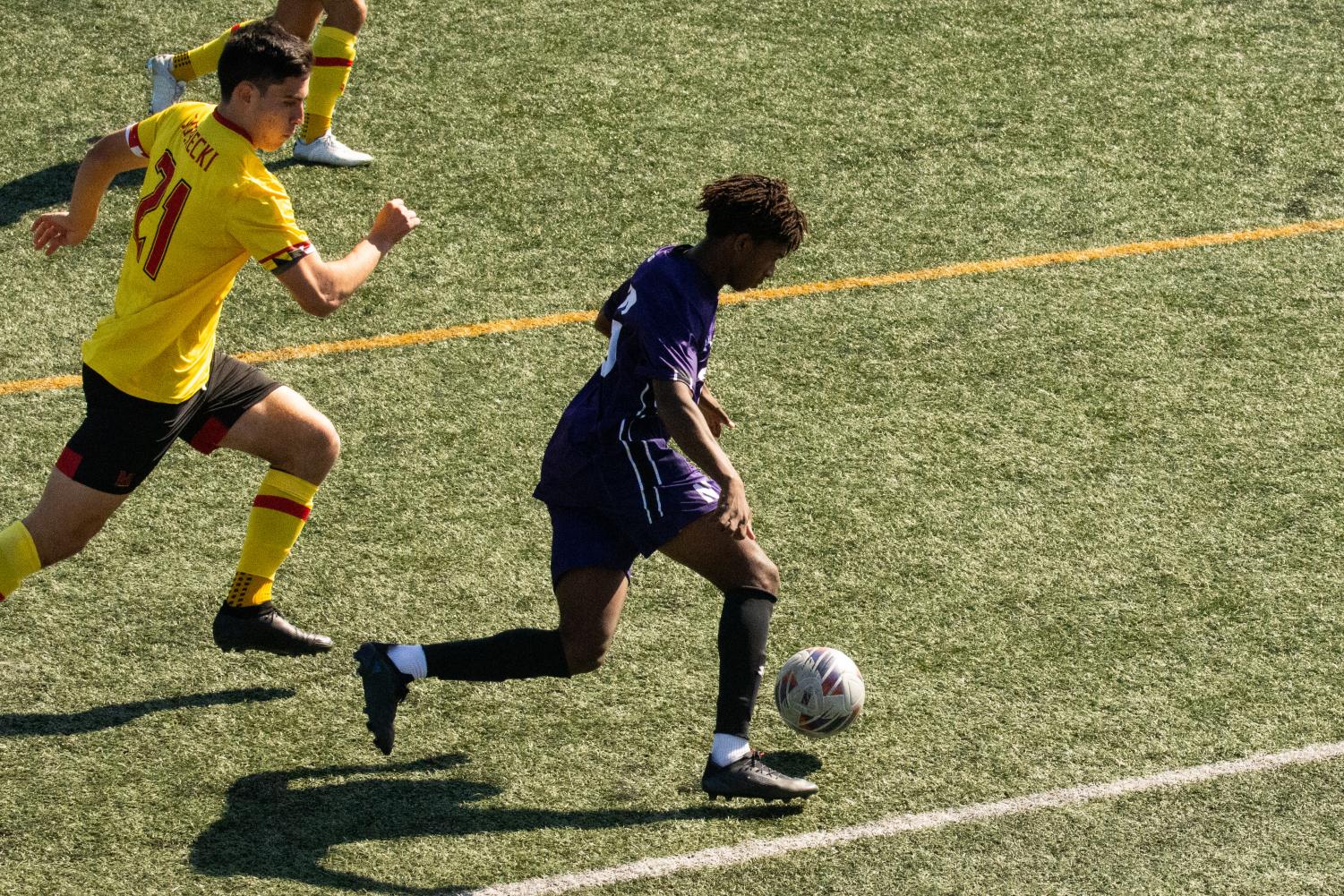 A+soccer+player+in+a+purple+jersey+and+purple+shorts+dribbles+a+ball.