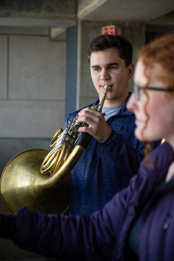A musician plays French horn in a concrete building.