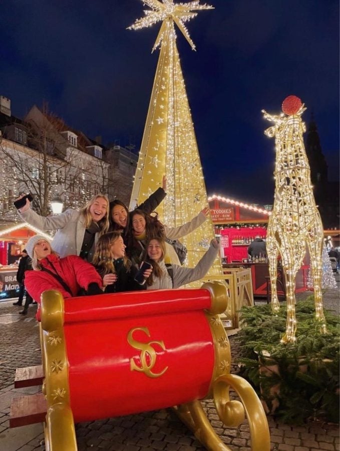 Six people sitting on a red sleigh in front of christmas decorations