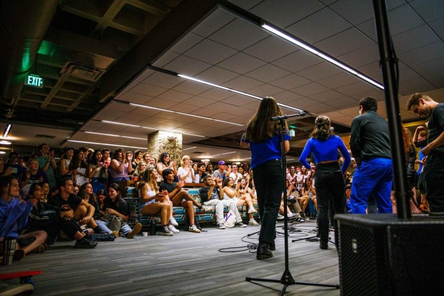 A group of students wearing blue sing in front of microphones to an applauding audience.