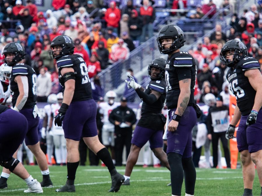 Players in black uniforms line up on a field before a play.