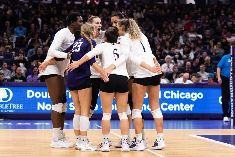 Volleyball players in white jerseys huddle together on a volleyball court.